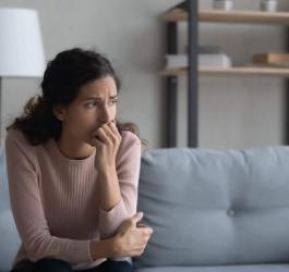 Smutna kobieta siedzi na kanapie, spogląda przez okno.