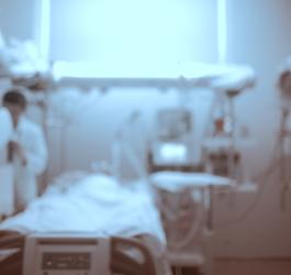 Rozmazane zdjęcie sali szpitalnej z pacjentem na łóżku i lekarzem przy aparaturze medycznej.