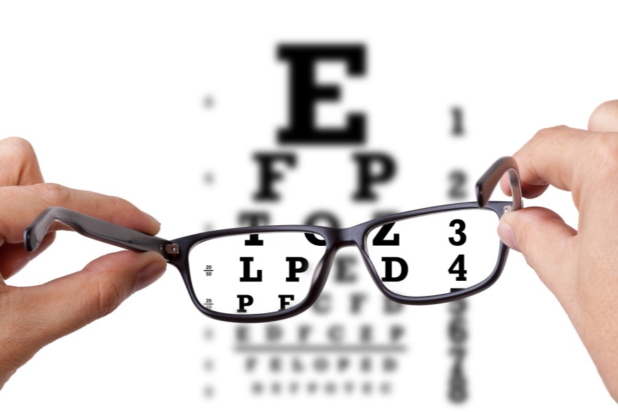 Pacjent trzyma okularu korekcyjne, w tle tablica okulistyczna.