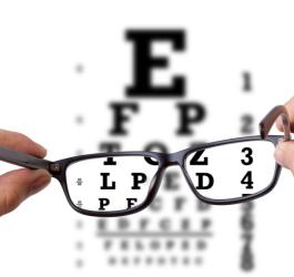 Pacjent trzyma okularu korekcyjne, w tle tablica okulistyczna.