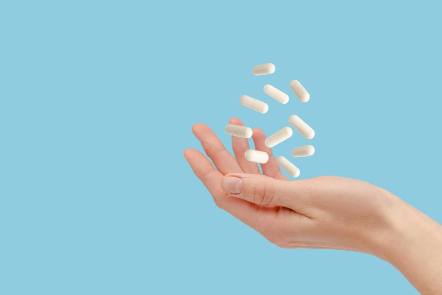 Kobieta podrzuca dłonią białe kapsułki zawierające probiotyk dopochwowy.