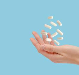 Kobieta podrzuca dłonią białe kapsułki zawierające probiotyk dopochwowy.