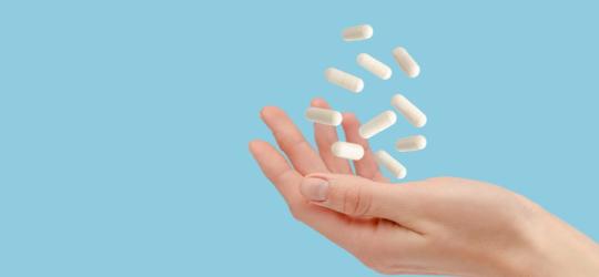 Kobieta podrzuca dłonią białe kapsułki zawierające probiotyk dopochwowy.