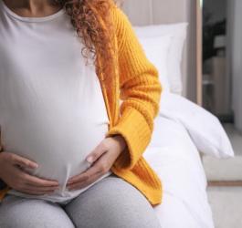 Ciężarna kobieta trzyma się za ciążowy brzuch.