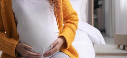 Ciężarna kobieta trzyma się za ciążowy brzuch.