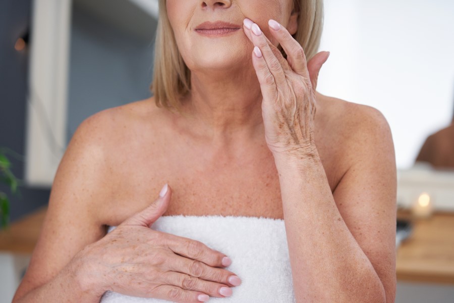 Dojrzała kobieta w trakcie pielęgnacji ciała i skóry twarzy.