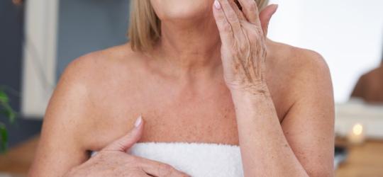 Dojrzała kobieta w trakcie pielęgnacji ciała i skóry twarzy.