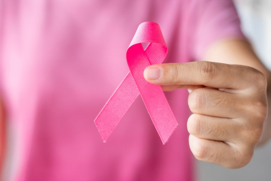Osoba w różowym fartuchu trzyma różową wstążkę, symbolizującą walkę z rakiem piersi.