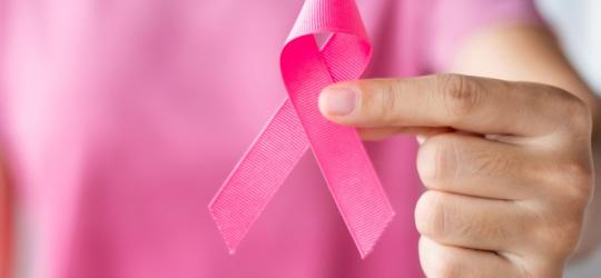 Osoba w różowym fartuchu trzyma różową wstążkę, symbolizującą walkę z rakiem piersi.