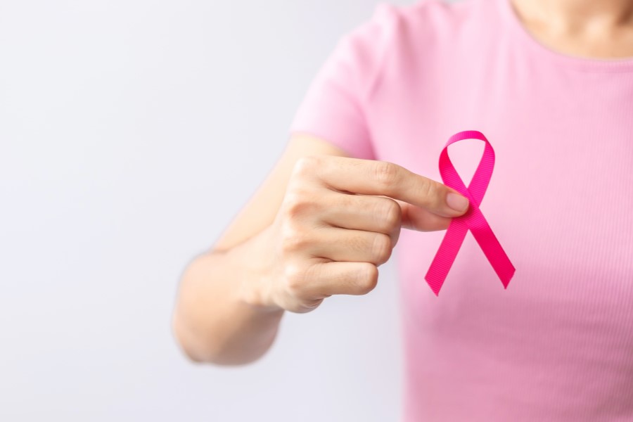Kobieta ma w dłoni różową wstążeczkę – symbol walki z rakiem piersi.
