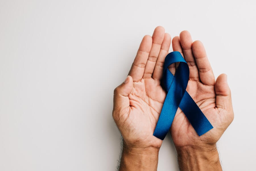 Mężczyzna trzyma w dłoniach niebieską wstążkę — symbol walki z rakiem prostaty.