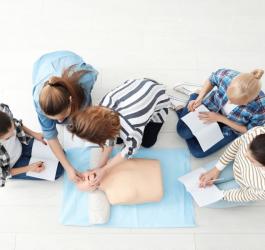 Grupa 5 osób podczas kursu resuscytacji krążeniowo-oddechowej. Robią notatki i ćwiczą na fantomie.