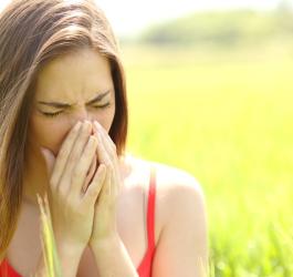 Młoda kobieta na łące. Wydmuchuje nos, bo zmaga się z objawami alergii na pyłki.