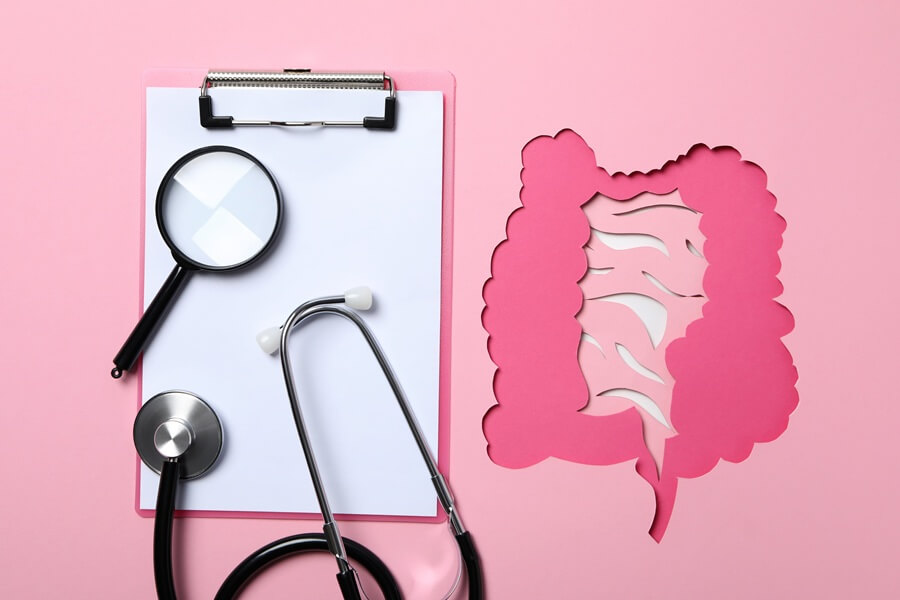 Papierowy model jelit obok notatnika, szkła powiększającego i stetoskopu lekarskiego.