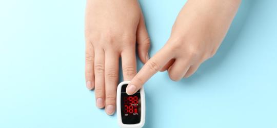 Kobieta ma na palcu pulsoksymetr, który mierzy saturację krwi.