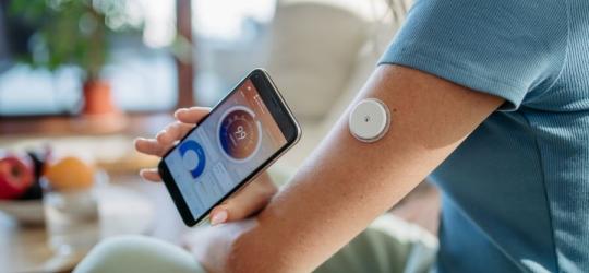 Osoba z założonym systemem CGM pokazuje na telefonie swoje wyniki glikemii.