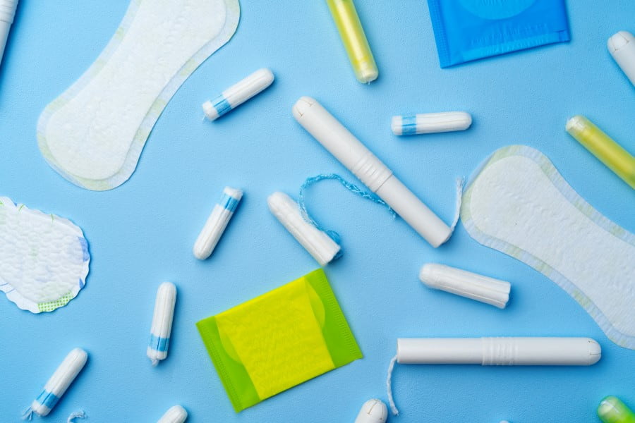 Rozmaite przybory higieniczne - podpaski, wkładki i tampony na niebieskim tle.