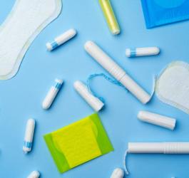 Rozmaite przybory higieniczne - podpaski, wkładki i tampony na niebieskim tle.