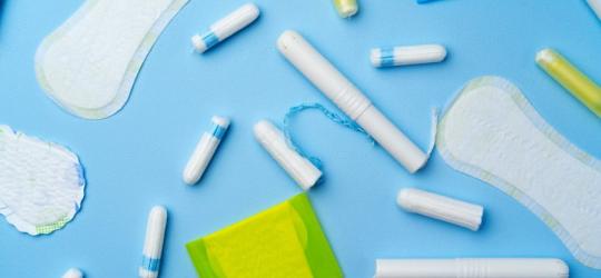 Rozmaite przybory higieniczne - podpaski, wkładki i tampony na niebieskim tle.
