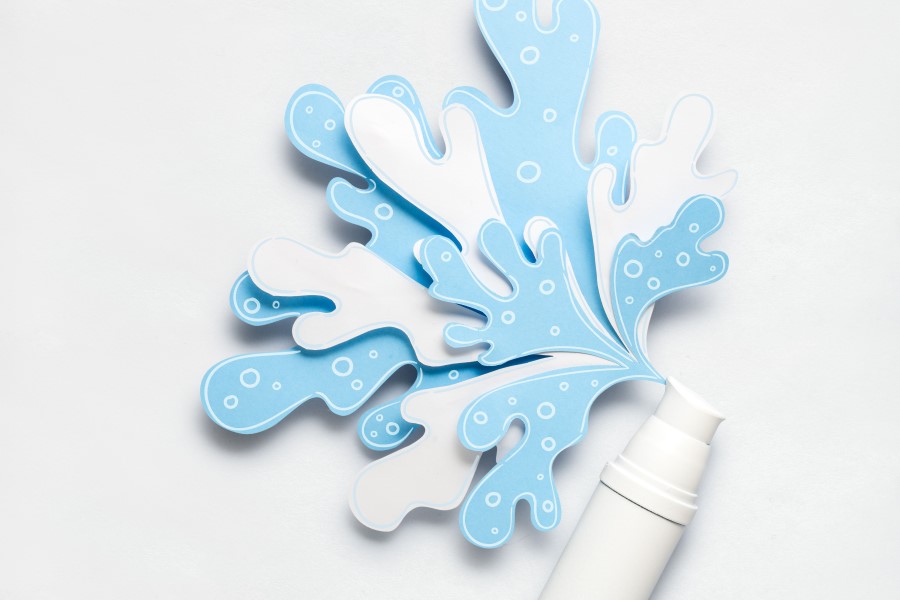 Biała buteleczka z wyciętą z papieru dekoracją w kształcie rozbryzgów wody.