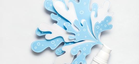 Biała buteleczka z wyciętą z papieru dekoracją w kształcie rozbryzgów wody.