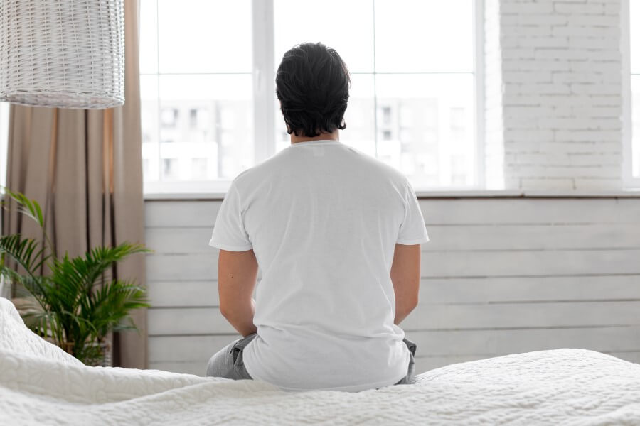 Zmartwiony zaburzeniami erekcji mężczyzna siedzi na skraju łóżka.