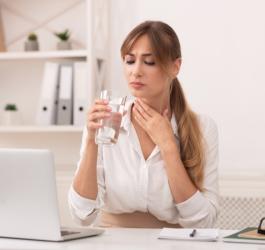 Kobieta pije wodę ze szklanki, odczuwa suchość w gardle i przełyku.
