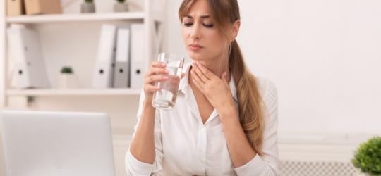 Kobieta pije wodę ze szklanki, odczuwa suchość w gardle i przełyku.