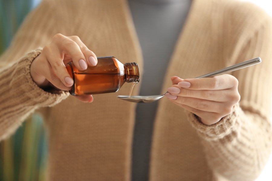 Kobieta nalewa na łyżeczkę syropu na łyżkę.