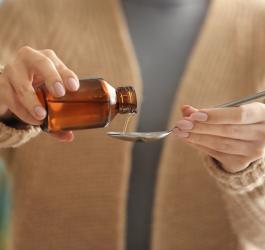 Kobieta nalewa na łyżeczkę syropu na łyżkę.