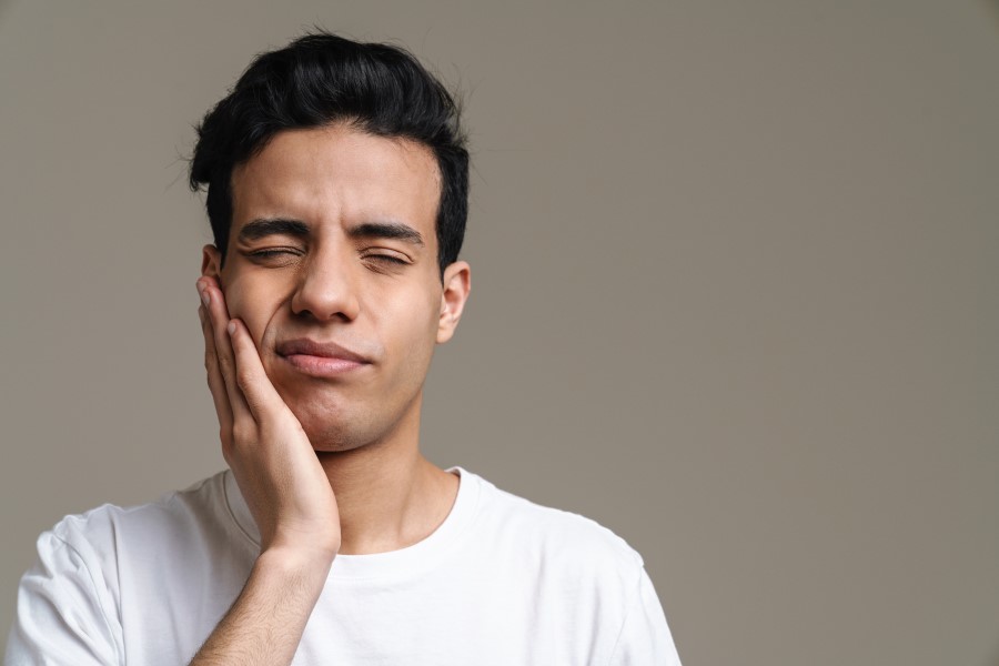 Mężczyznę boli szczęka, przyciska dłoń do twarzy.