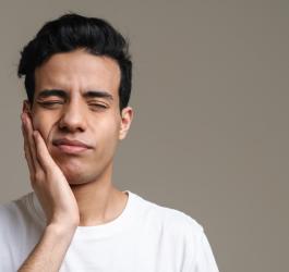 Mężczyznę boli szczęka, przyciska dłoń do twarzy.