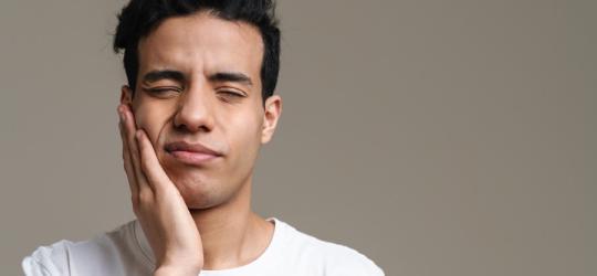 Mężczyznę boli szczęka, przyciska dłoń do twarzy.
