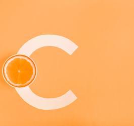 Literka C i połówka pomarańczy na pomarańczowym tle, symbolizujące witaminę C.