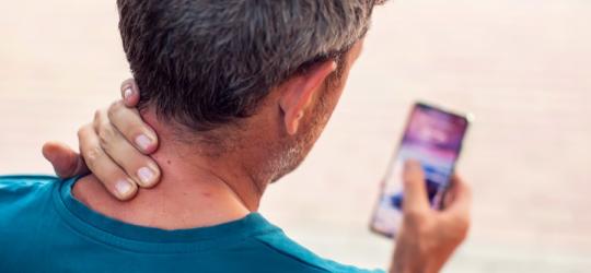 Mężczyzna korzysta ze smartfona, dokucza mu tzw. szyja smartfonowa.