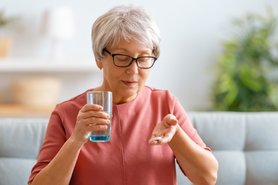 Starsza kobieta planuje przyjąć tabletkę na uspokojenie i popić ją szklanką wody.