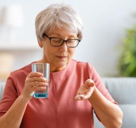 Starsza kobieta planuje przyjąć tabletkę na uspokojenie i popić ją szklanką wody.