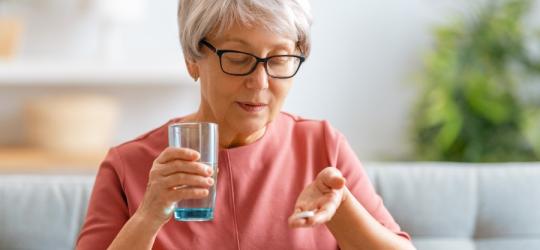 Starsza kobieta planuje przyjąć tabletkę na uspokojenie i popić ją szklanką wody.