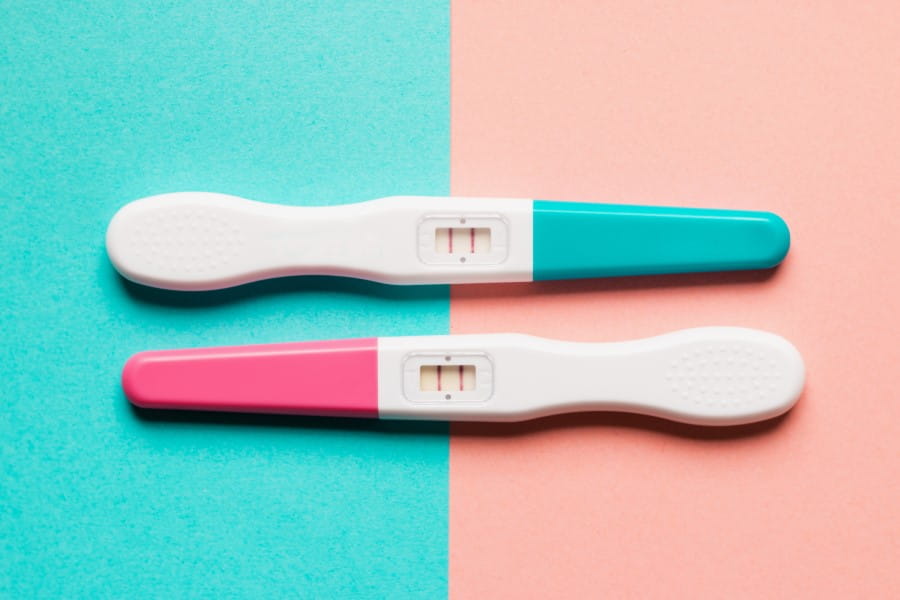 Dwa pozytywne testy ciążowe na turkusowo-różowym tle.