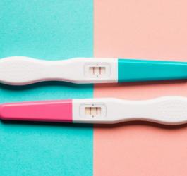 Dwa pozytywne testy ciążowe na turkusowo-różowym tle.