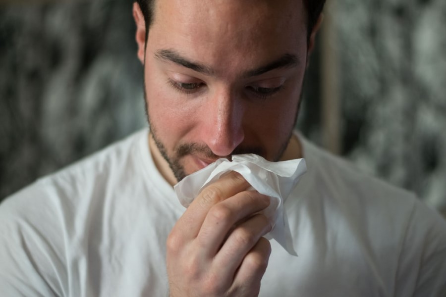 Mężczyzna wydmuchuje nos w chusteczkę higieniczną, męczy go katar.