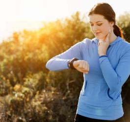 Młoda kobieta ręcznie mierzy swoje tętno maksymalne na tętnicy szyjnej, korzysta tez ze smartwatcha.