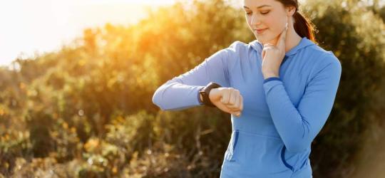 Młoda kobieta ręcznie mierzy swoje tętno maksymalne na tętnicy szyjnej, korzysta tez ze smartwatcha.