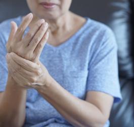 Kobieta trzyma się za prawą dłoń. Cierpi na tężyczkę.