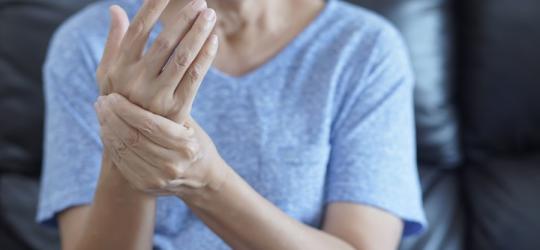 Kobieta trzyma się za prawą dłoń. Cierpi na tężyczkę.