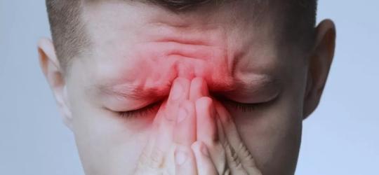 Mężczyzna trzyma się za nasadę nosa.