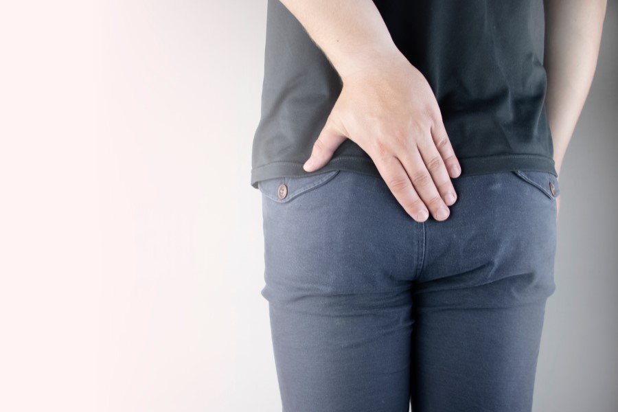 Mężczyzna trzyma rękę w okolicy kości ogonowej, czyli tam, gdzie może powstać torbiel włosowa.