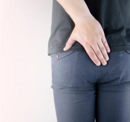 Mężczyzna trzyma rękę w okolicy kości ogonowej, czyli tam, gdzie może powstać torbiel włosowa.