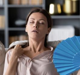 Kobieta doświadcza uderzenia gorąca, schładza się przy pomocy wachlarza.