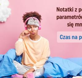 Kobieta w pidżamie, siedzi w łóżku, ma na głowie opaskę na oczy i słuchawki.